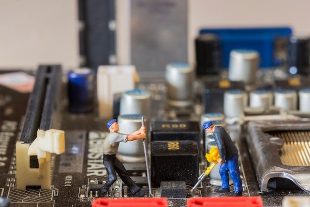 Miniature workers repairing a computer motherboard, illustrating computer system maintenance and repair services.